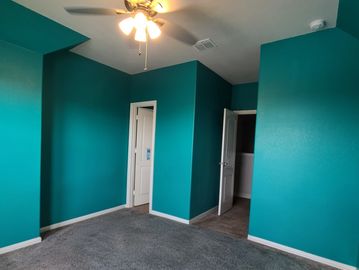 Empty teal-colored room with gray carpet and ceiling fan.