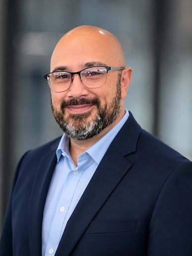 Smiling bald man with glasses in a blue suit and light blue shirt.