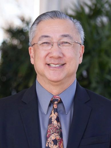 Smiling middle-aged man in glasses and suit outdoors.