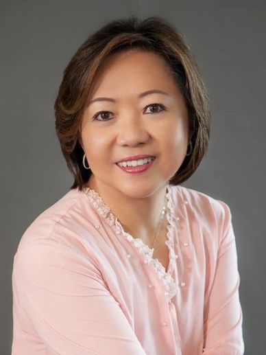 Smiling woman in pink blouse against gray background.