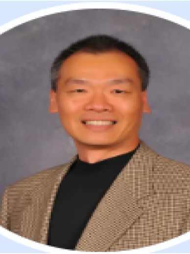 Man smiling, wearing a checked blazer and black shirt.