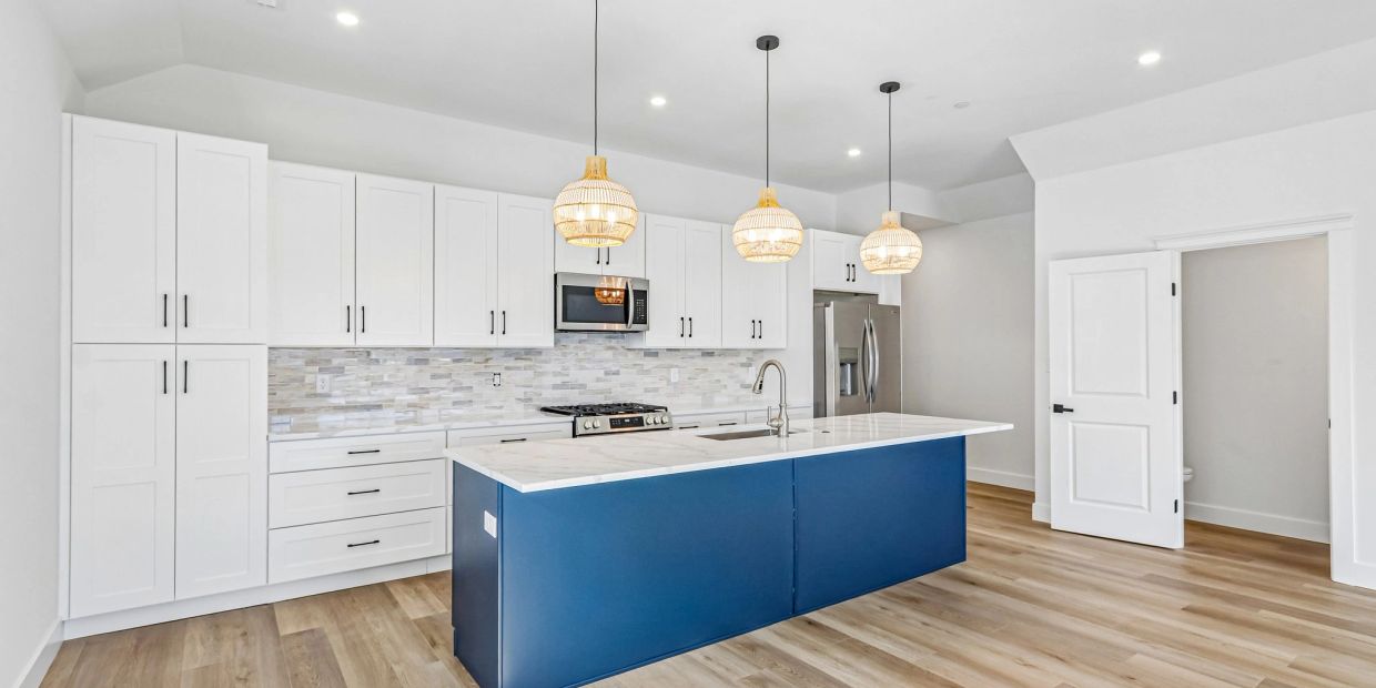 Modern kitchen with white cabinets and a blue island under pendant lighting.