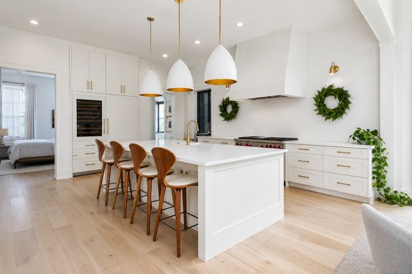 Modern white kitchen with wooden chairs and pendant lights.