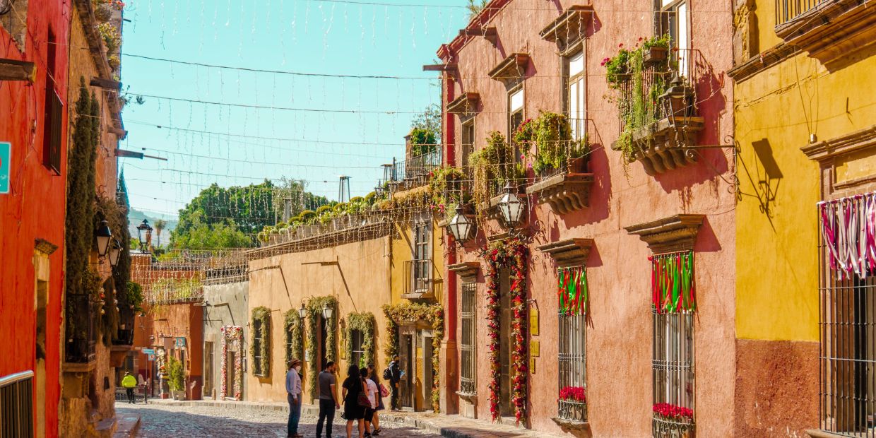 Colorful street with hanging plants and people walking.