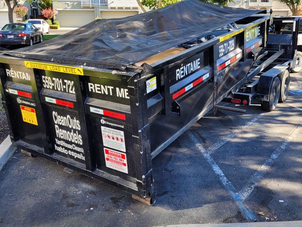 Large black dumpster trailer for rent with bilingual signage in a neighborhood.