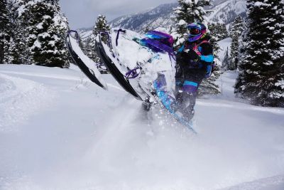 Person doing a wheelie on a snowmobile in snowy landscape.