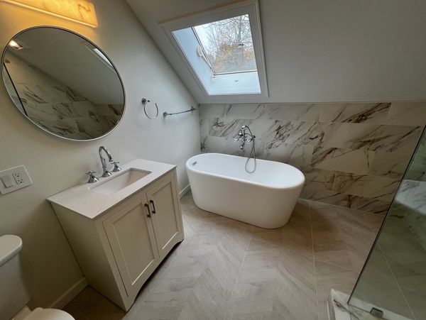 Modern bathroom with freestanding tub, round mirror, and skylight.