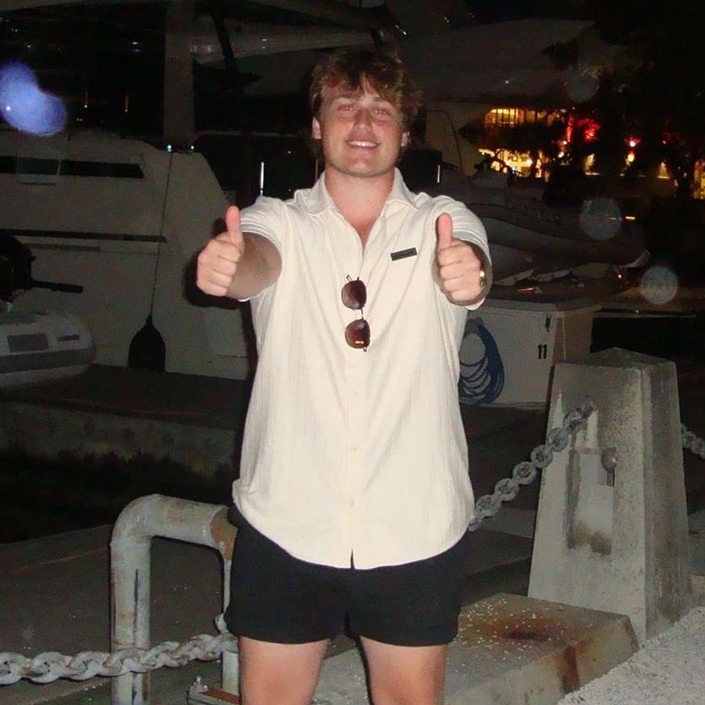 Young man giving thumbs up at night near boats.