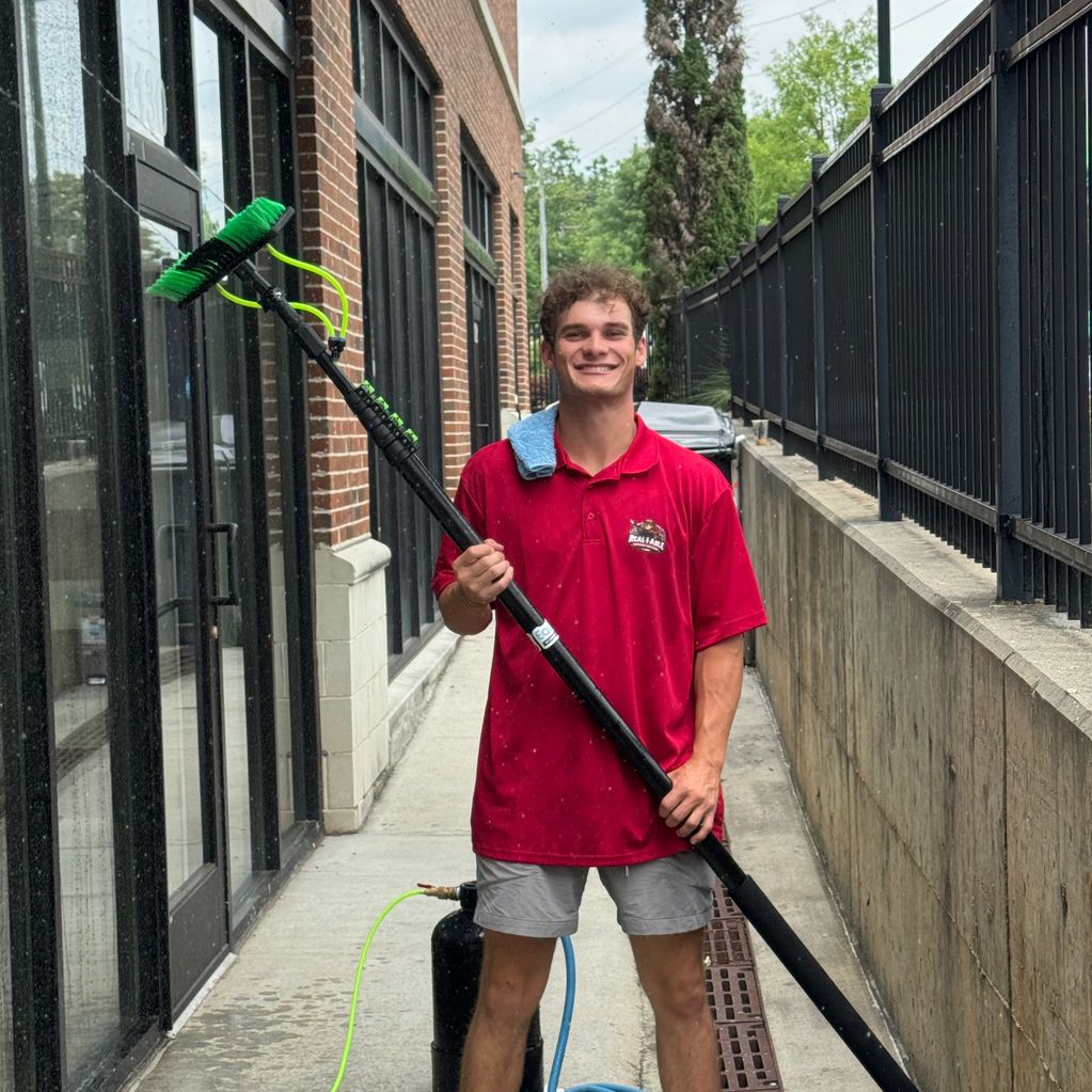 Man in red shirt holding a long cleaning brush, standing outside a building.