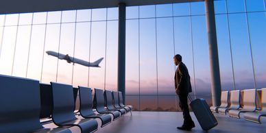 Businessman watches a plane take off from an empty airport lounge at sunset.