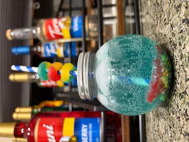 Colorful drink in a round glass jar with a striped straw and candy garnish.
