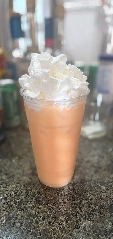 Orange iced drink topped with whipped cream in a clear plastic cup.