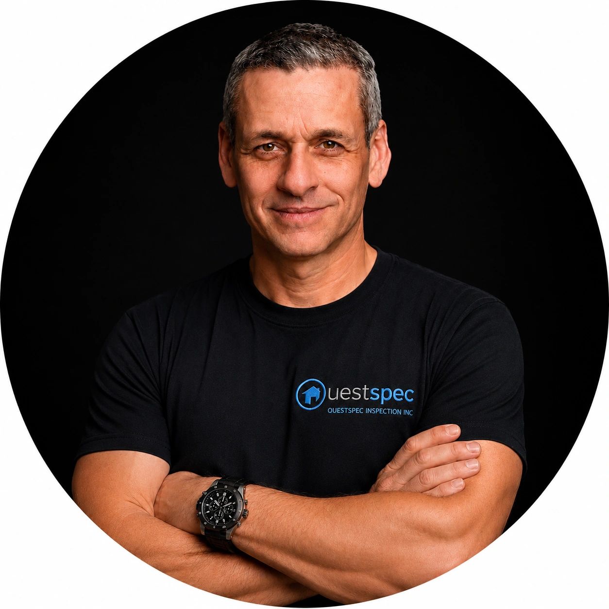 Confident man with arms crossed wearing a black QuestSpec t-shirt against a black background.