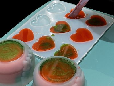 Pouring colorful liquid into heart-shaped molds for making decorative resin pieces.