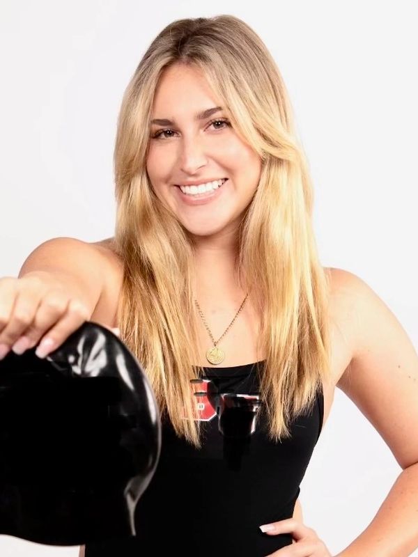 Smiling blonde woman holding a kettlebell, wearing a black tank top.