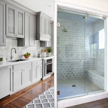 Modern gray kitchen adjacent to a glass shower enclosure.