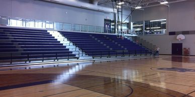 Empty indoor basketball court with purple bleachers and polished wooden floor.