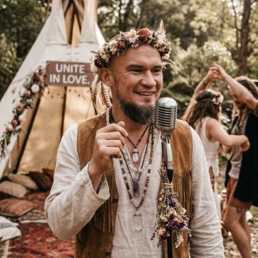 Man in floral crown speaking into microphone at outdoor event.