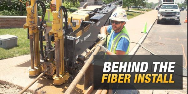 Worker installs fiber optic cables using heavy machinery on a sunny day.