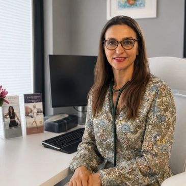 A female doctor with glasses and stethoscope sitting at her office desk.