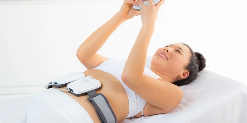 Woman lying down with body contouring devices on her abdomen.