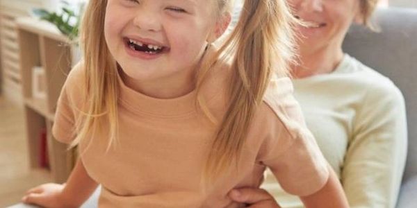 A joyful young girl with a woman smiling behind her indoors.