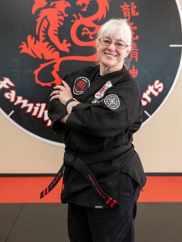 Smiling martial artist in black gi and black belt standing confidently indoors.