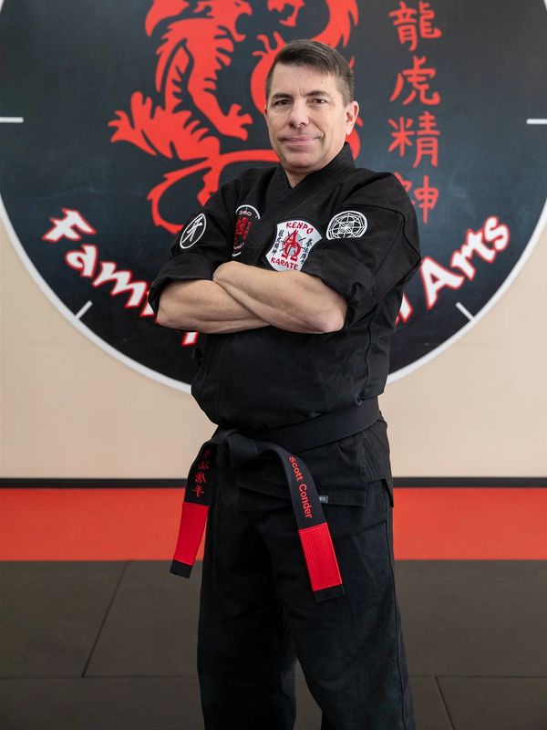 Martial artist in black gi with red and black belt posing confidently.