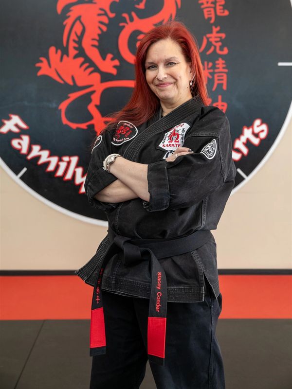 Confident martial artist in black gi with red hair and black belt at dojo.