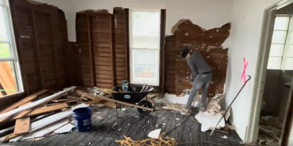 Person demolishing interior wall during room renovation.