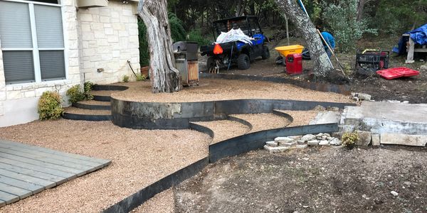 A backyard landscaping project with gravel paths, trees, and construction equipment.