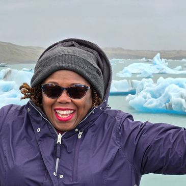 A joyful woman in winter clothes near icy waters with floating icebergs.