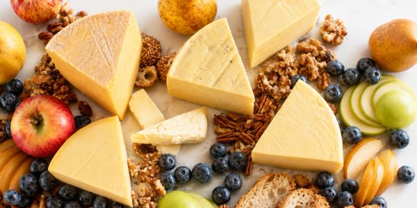Assorted cheeses with fruits and nuts on a white surface.