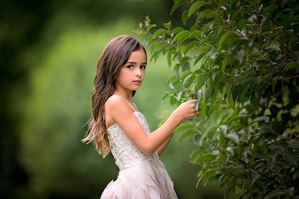 Young girl in a white dress among green foliage.