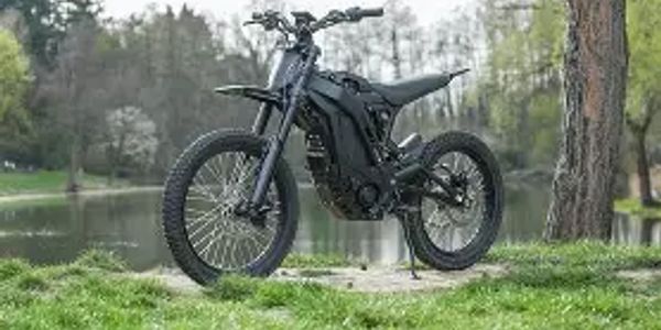 Sleek black electric dirt bike parked on grass by a lake.
