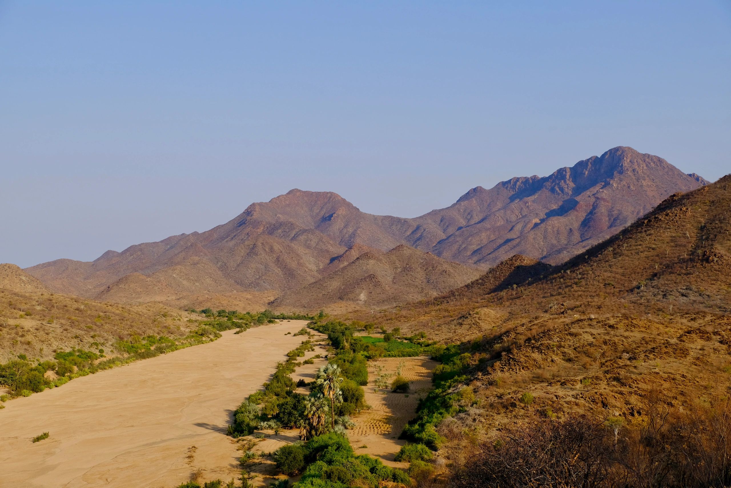 Mountain range with dry riverbed and sparse vegetation.