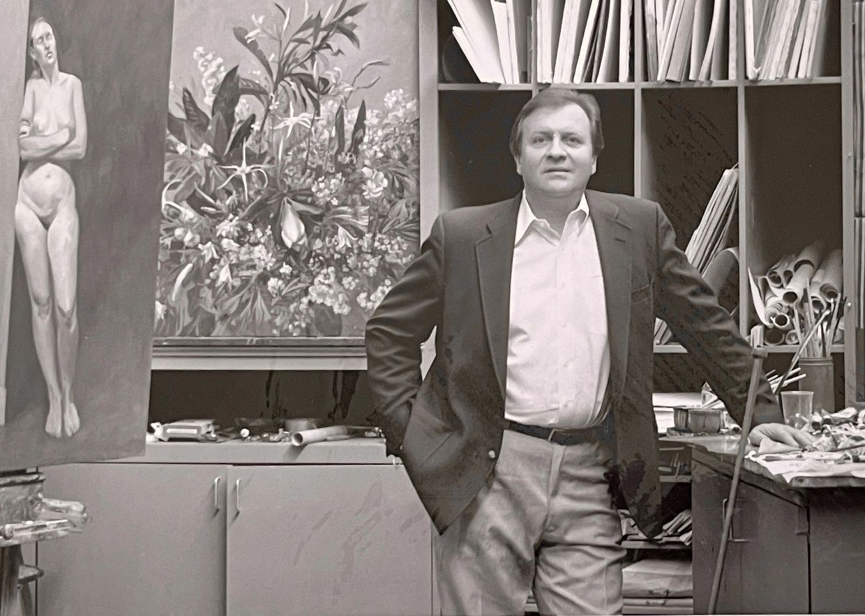 Man standing in an art studio surrounded by paintings and supplies.