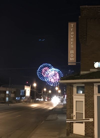 "Travers Row" sign at night with heart-shaped fireworks in the background over a street