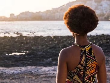 Person with afro hairstyle looking at the sea during sunset.