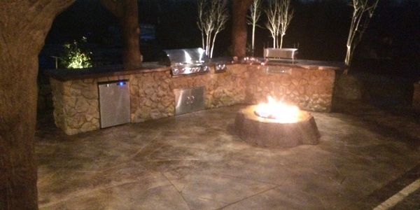 An amazing outdoor kitchen with a custom pergola with real looking concrete trees and stump fire pit