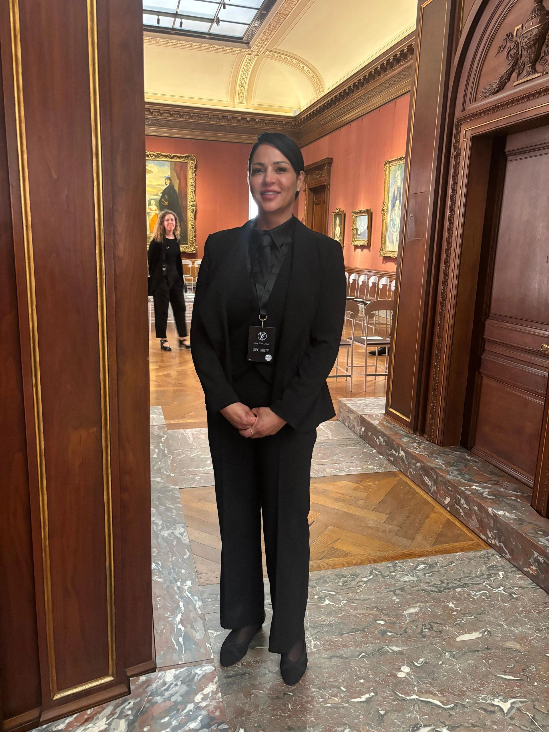 A security guard in black suit stands in an elegant art gallery room.