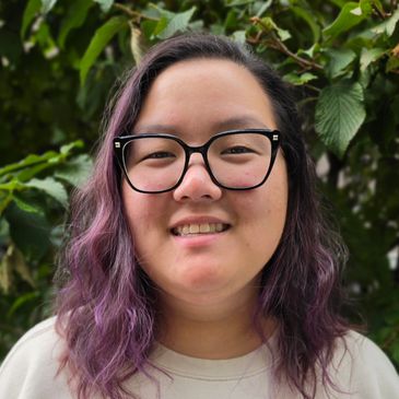 Smiling person with glasses and purple hair.