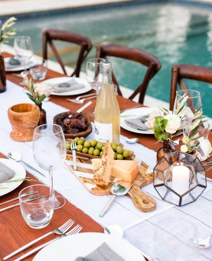 Elegant outdoor table setting with cheese, olives, and candle by the pool.