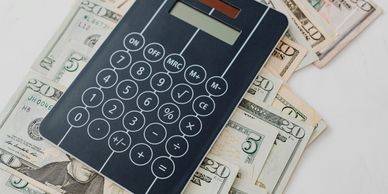 A black calculator on top of scattered US dollar bills.