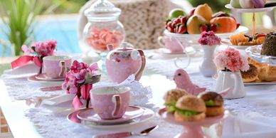 A beautifully set table with pink-themed tea cups, flowers, and snacks.