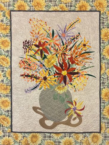 Colorful floral quilt with sunflowers and a vase.