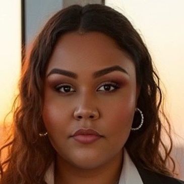 Confident woman with wavy hair and hoop earrings, dressed in business attire.