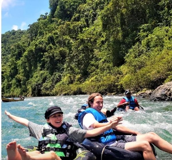 People enjoying river tubing surrounded by lush greenery and clear blue sky.