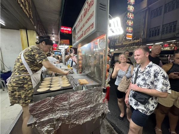 Street vendor cooking treats while tourists watch and wait.