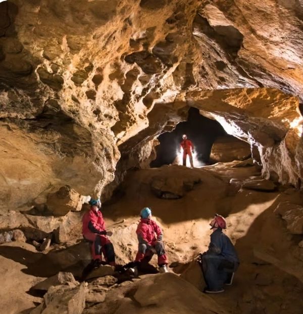 Group exploring a large, illuminated cave with rocky formations.